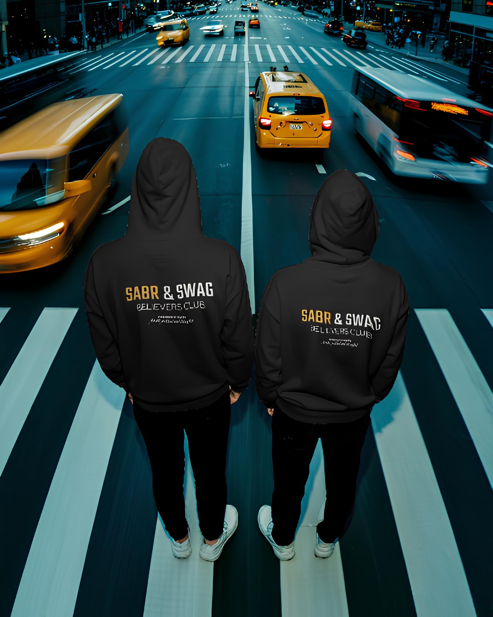 Two people wearing black hoodies with 'Sabr & Swag' text on a city street with taxis.